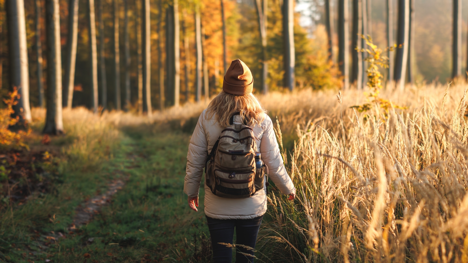 A woman walks along a wooded path in the fall.