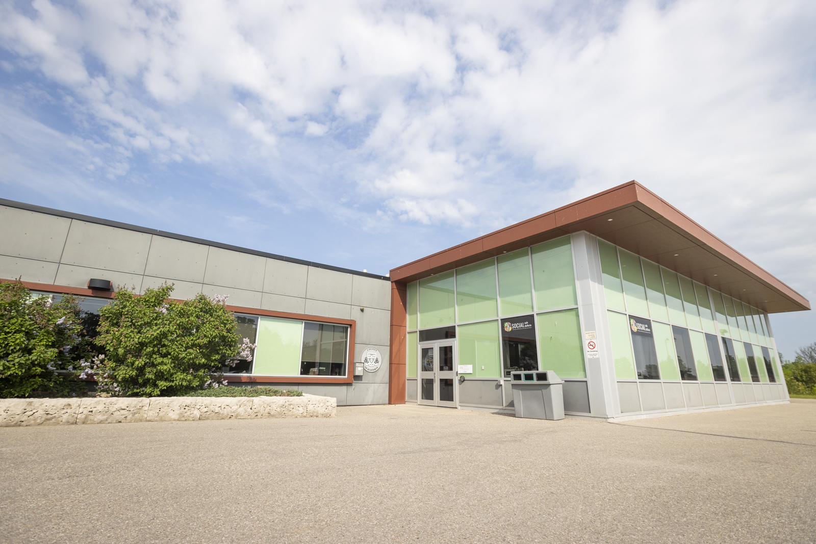 A one story building with a flower bed, large windows with green glass and grey stucco.