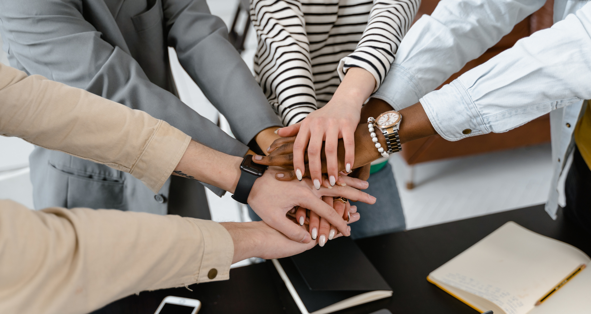 A group of people standing at a desk put their hands together in cooperation