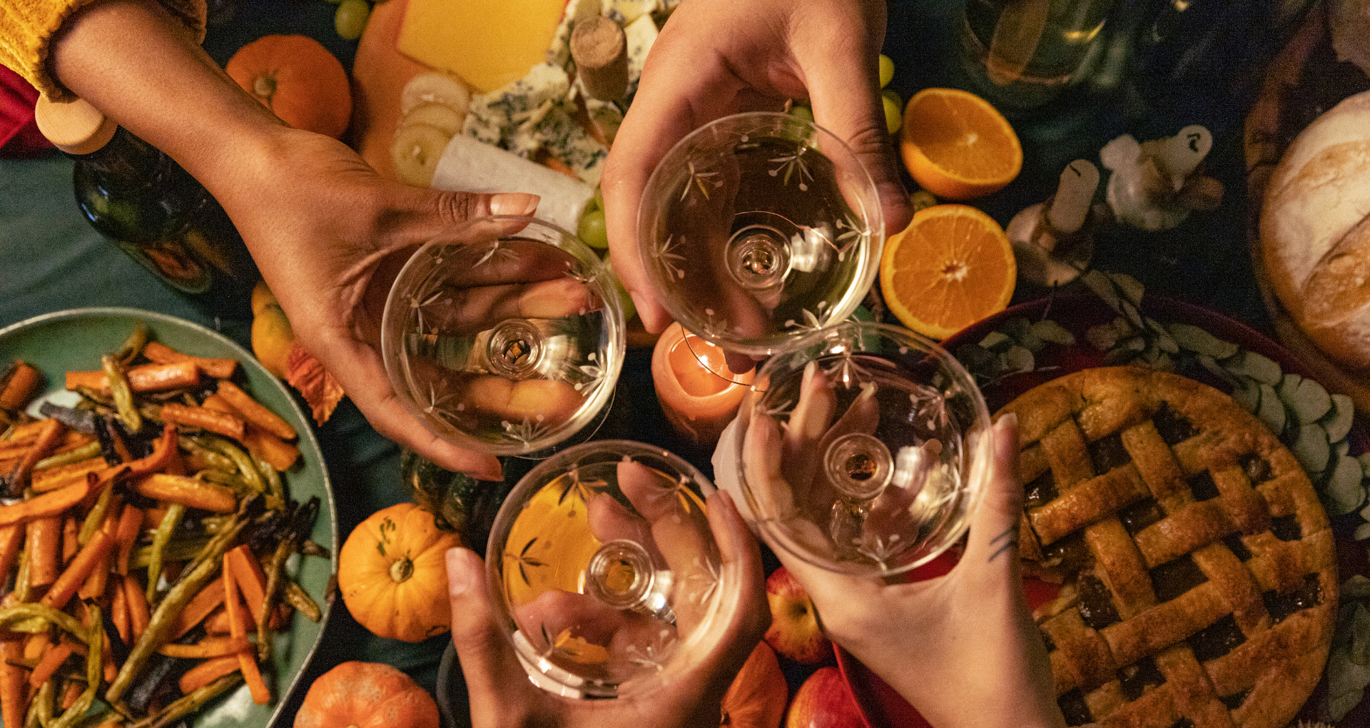 Hands holding drink glasses clink them together above a holiday meal