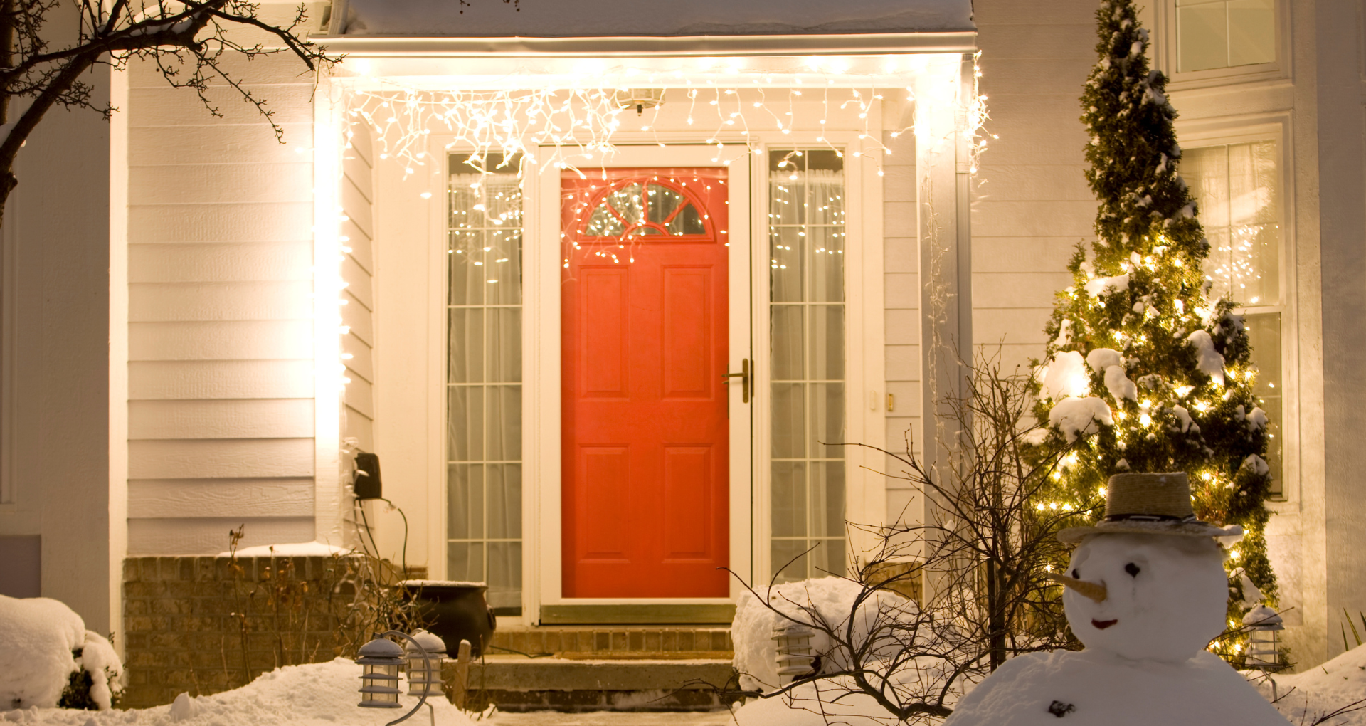 a house's red front door at night, lit by icicle lights and surrounded by snow