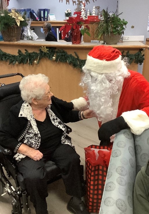 Santa Claus sits with a senior, talking and offering a gift